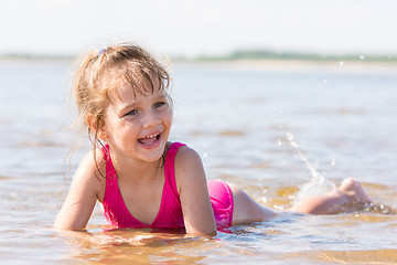 Image showing Five-year girl lies in water in the shallows of the river, laughing and looking to the left