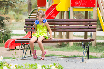 Image showing Upset girl bit her lip while sitting on the bench on the background of the playground