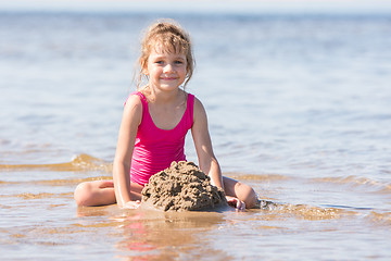 Image showing Five-year girl in a pink bathing suit playing in the sand in the shallows of the river