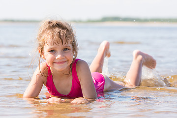 Image showing Five-year girl lies in water in the shallows of the river and looking at the frame