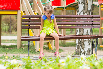 Image showing Crying girl sitting on the bench on the background of the playground