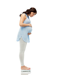 Image showing happy pregnant woman measuring weight on scales