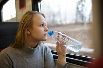 Image showing Woman drinking water and looking out train window