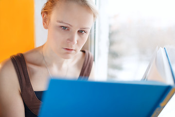 Image showing Young woman reading a book with blue cover