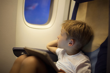 Image showing Boy in plane looking out illuminator with pad on lap