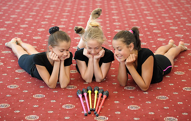 Image showing Three girls on the floor looking at Indian clubs