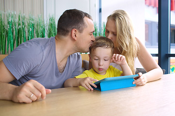 Image showing Parents kissing son playing on pad