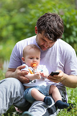 Image showing Father using a mobile with baby on his lap