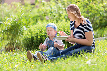 Image showing Cute little boy being fed outdoors on the grass