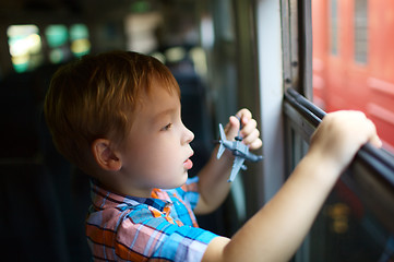 Image showing Little boy with toy looking out of train window