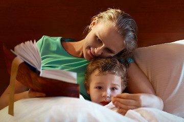 Image showing Young mother reading to her child in bed