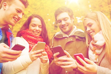 Image showing smiling friends with smartphones in autumn park