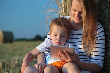 Image showing Mother and son with pad sitting by hay roll in the field