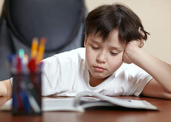 Image showing School boy studies hard over his book at home.