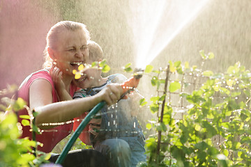 Image showing Laughing mother and son playing with a sprinkler