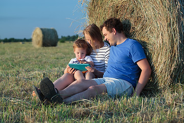 Image showing Family of three with pad in the field with hay rolls