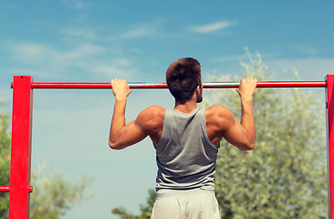 Image showing young man exercising on horizontal bar outdoors