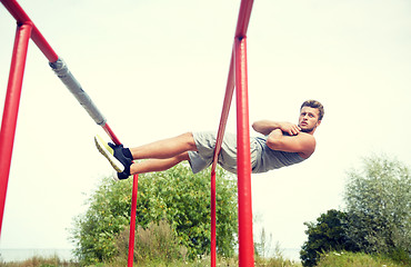 Image showing young man doing sit up on parallel bars outdoors