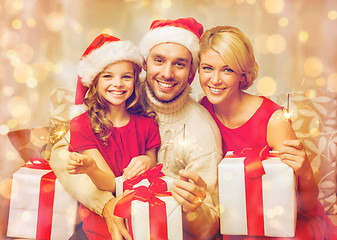 Image showing smiling family holding gift boxes and sparkles