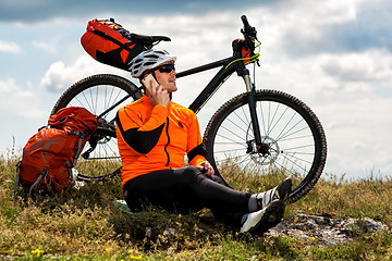 Image showing Young man sitting near the cycle on a green meadow