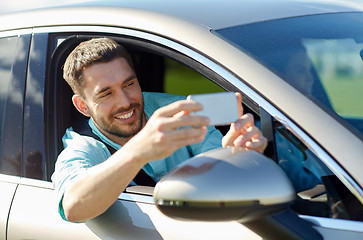 Image showing happy smiling man with smartphone driving in car