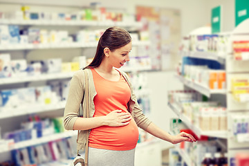 Image showing happy pregnant woman choosing medicine at pharmacy