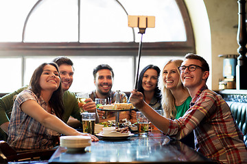 Image showing happy friends with selfie stick at bar or pub