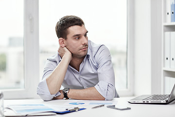 Image showing bored businessman with laptop and papers at office