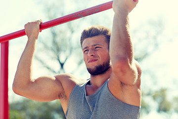 Image showing young man exercising on horizontal bar outdoors