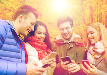 Image showing smiling friends with smartphones in city park