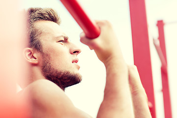 Image showing young man exercising on horizontal bar outdoors