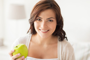 Image showing smiling young woman eating green apple at home