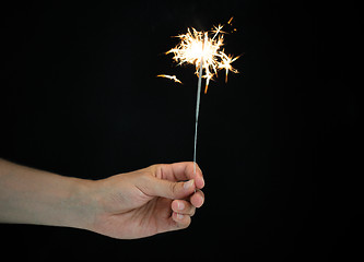 Image showing hand holding sparkler over black background