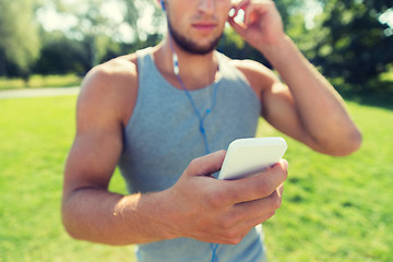 Image showing young man with earphones and smartphone at park