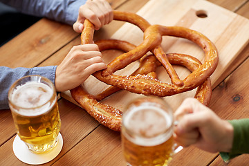 Image showing close up of men drinking beer with pretzels at pub