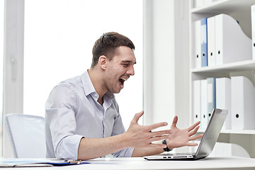 Image showing angry businessman with laptop and papers in office