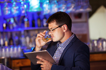 Image showing Businessman with tablet drinking whisky in bar