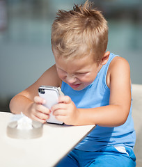 Image showing Young boy peering closely at a mobile phone