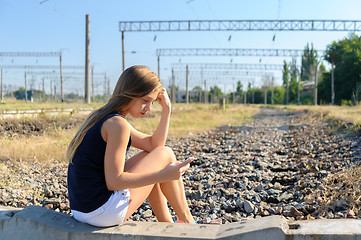 Image showing Teenager girl with mobile sitting on unfinished rail track