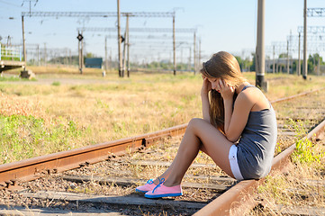 Image showing Upset teenager girl sitting on rail track in countryside