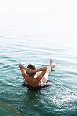 Image showing Back view of relaxing woman floating on inflatable ring