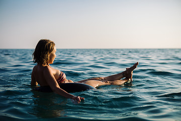 Image showing Back view of relaxing woman floating on inflatable ring