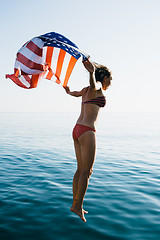 Image showing Young woman in bikini jumping in water with American flag