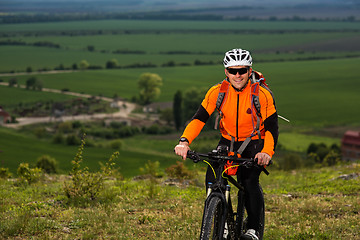 Image showing Young man cycling on a rural road through green meadow