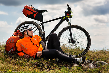 Image showing Young man sitting near the cycle on a green meadow