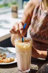 Image showing Female hand stirring cold drink in glass with straw