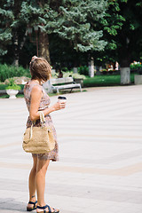 Image showing Young brunette woman with coffee cup walking in city