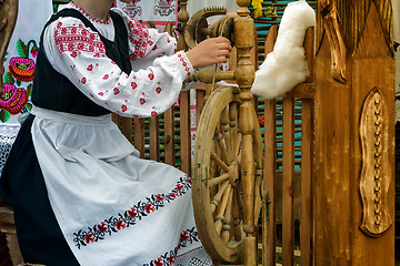 Image showing Young woman spinning thread on a spinning wheel.