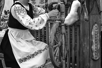 Image showing Young woman spinning thread on a spinning wheel. Black-and-white