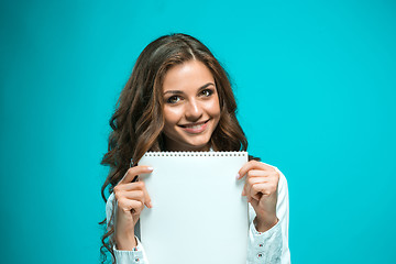 Image showing The smiling young business woman with pen and tablet for notes on blue background